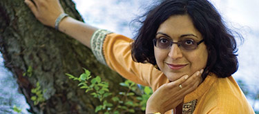 Umrigar in a yellow shirt leaning against/sitting in a tree with her chin in one hand